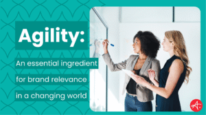 Two professional women collaborate at a whiteboard, discussing ideas and strategies, representing brand agility and adaptability in a modern business setting. Text overlay reads: Agility – An essential ingredient for brand relevance in a changing world.