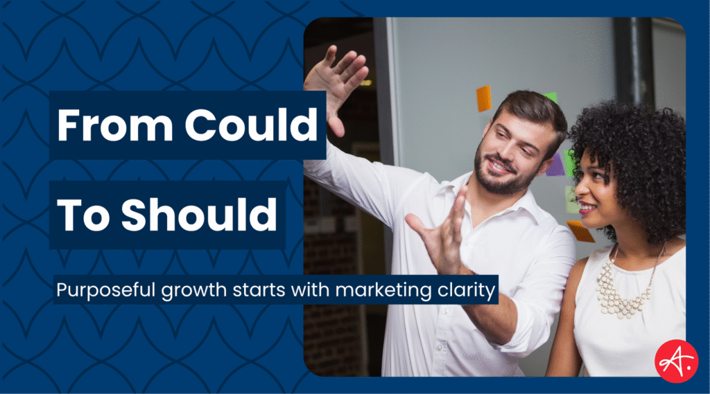 Two professionals brainstorm together in an office, smiling as they discuss marketing ideas with sticky notes in the background. Text overlay reads: From Could To Should – Purposeful growth starts with marketing clarity.