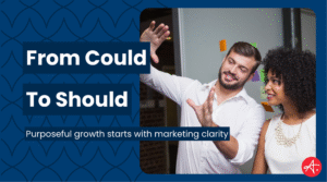 Two professionals brainstorm together in an office, smiling as they discuss marketing ideas with sticky notes in the background. Text overlay reads: From Could To Should – Purposeful growth starts with marketing clarity.