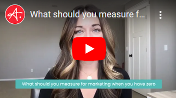 A smiling woman with long brown hair wearing a black top, speaking to the camera in a neutral-toned room. A text overlay reads, "What should you measure for marketing when you have zero."