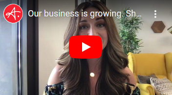 A video thumbnail of a professional woman speaking, with a red YouTube play button overlay in the center. The background includes a yellow chair, green plants, and modern hexagonal wall decor. The title 'Our business is growing. Sh...' is partially visible at the top.