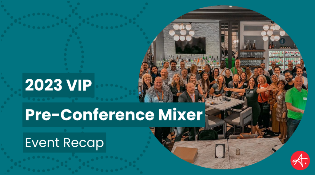 A lively group of conference attendees gathered in a modern bar setting during the 2023 VIP Pre-Conference Mixer. People are smiling, mingling, and posing for a group photo, surrounded by a well-stocked bar and elegant lighting.